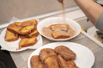 Close-up of freshly fried torrijas being coated in cinnamon sugar on a kitchen counter.