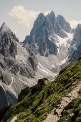 Breathtaking alpine landscape featuring towering jagged peaks, lush green slopes, and a rugged hiking trail. A stunning view of the majestic Dolomites, Italy perfect for adventure and nature lovers
