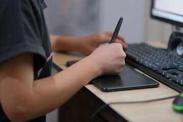 A hand holds a stylus and draws on a graphics tablet connected to a computer.
