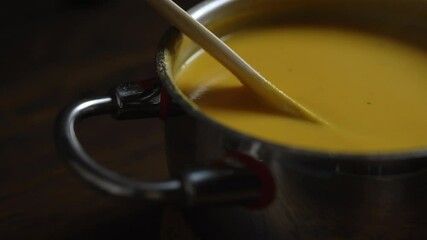 Pumpkin soup in a saucepan. Stirring with a wooden spoon. - Powered by Adobe