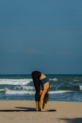 Young caucasian female practicing yoga on beach with ocean waves in background