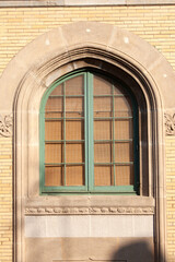 Arched window with divided panes and green trim. Classic architectural style, vintage building, and a glimpse of interior blinds.