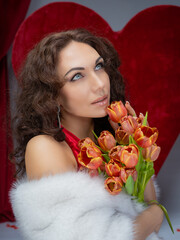 A beautiful brunette woman in an elegant red evening gown holding a delicate bouquet of fresh tulips. She exudes grace and charm, with a confident smile and a sophisticated, feminine look, perfect for