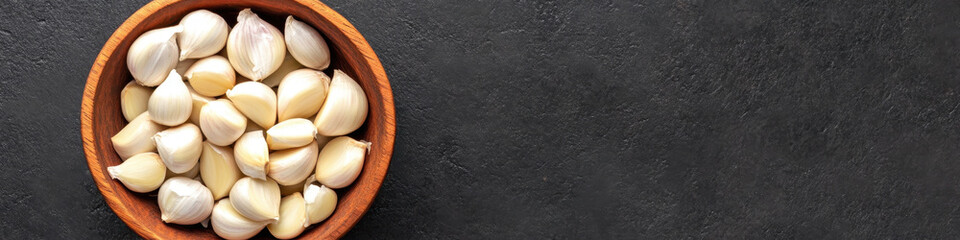 Fresh organic garlic cloves in wooden bowl on dark surface, showcasing their natural beauty and texture. Perfect for culinary use or decoration