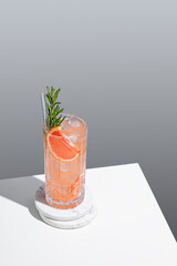 Refreshing cocktail with grapefruit, rosemary and ice in a glass on a gray background with shadow.