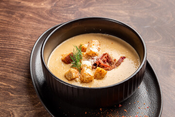 A rich, creamy soup served in a black bowl, garnished with croutons and fresh herbs. The rustic wooden background enhances the appetizing presentation of this delicious dish.