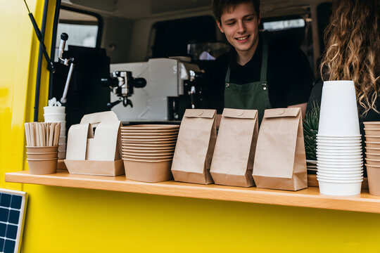 Bright yellow food truck serving drinks with two smiling servers in casual attire at a bustling outdoor location during the day. Two young servers, a man and a woman, smile while holding paper cups. 