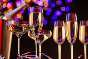 Champagne in glasses and party streamers against black background with blurred lights