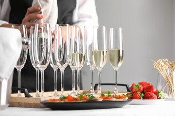 Waiter with bottle of drink, closeup. Champagne in glasses, strawberries and canapes on table