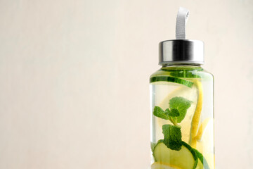 Lemon water with mint and slices of cucumber in bottle on beige background, closeup. Space for text