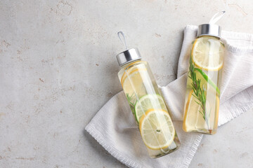 Lemon water with lime and rosemary in bottles on grey table, top view. Space for text