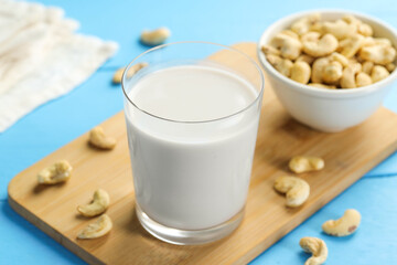 Fresh cashew milk in glass and nuts on light blue wooden table, closeup