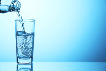 Pouring soda water from bottle into glass on light blue background, closeup. Space for text