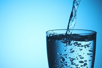 Pouring refreshing soda water into glass on light blue background, closeup. Space for text