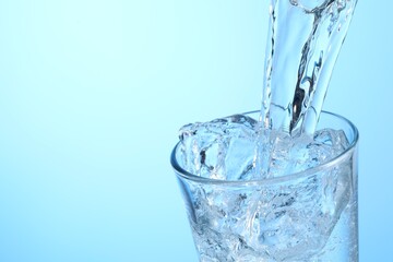 Pouring refreshing soda water into glass on light blue background, closeup. Space for text