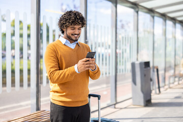 Man holding phone while standing at public transport stop. Passenger buys tickets remotely online,...