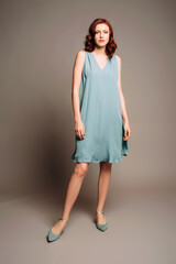 Beautiful young ginger woman in a midi dress and blue shoes on grey background at studio. Female...