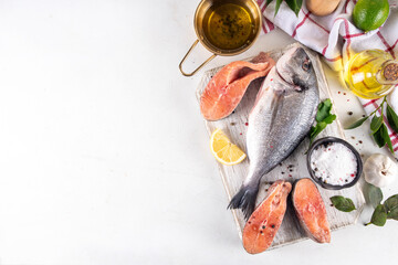 Raw fish and seafood cooking background, various fresh whole and sliced fish with spices, lemon, olive oil for preparation dinner, white table background copy space