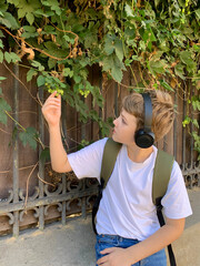 A young boy with short brown hair inspects small green berries growing on a vine by a wooden fence....