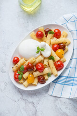 Pasta with burrata cheese, roasted cherry tomatoes and basil, vertical shot on a white stone background, high angle view