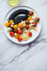 Plate with roasted cherry tomatoes, spaghetti and cheese, vertical shot on a white stone background with space, flat lay