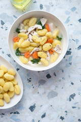 Bowl with creamy chicken gnocchi soup, vertical shot on a white and blue granite background with space, above view
