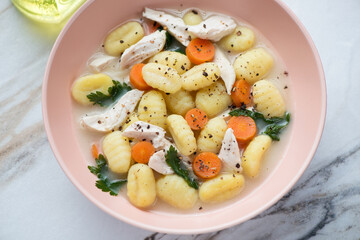 Creamy soup with chicken meat and potato gnocchi served in a roseate bowl, horizontal shot, middle close-up, selective focus