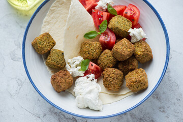 Falafel served with tomatoes, cheese and flat bread in a white and blue plate, horizontal shot, middle close-up