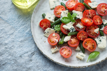 Salad with cherry tomatoes, green beans and blue cheese served on a grey plate, closeup, selective focus, horizontal shot