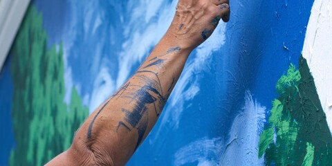 Artist's Arm Creating a Vibrant Mural. An artist's paint-splattered arm works on a colorful mural, showcasing creativity and expression in a dynamic urban art scene.