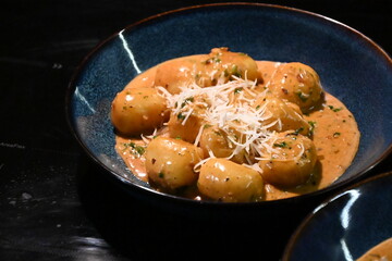 color photo of a dish of potato gnocchi sprinkled with parmesan, in a pepper sauce, with herbs, traditional homemade tasty food, close up view