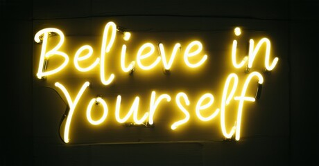 Neon words believe in yourself flashing with bright yellow, emitting vibrant, colorful illumination against a dark background, creating an empowering and motivating scene