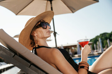 Side view, lying down with cocktail in hand. Beautiful young woman is at resort, vacation