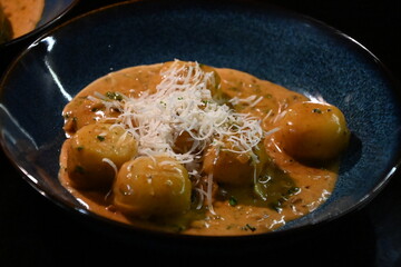 color photo of a dish of potato gnocchi sprinkled with parmesan, in a pepper sauce, with herbs, traditional homemade tasty food, close up view