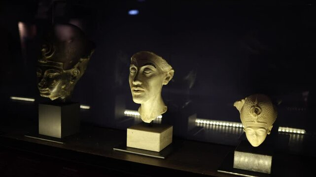 A collection of three ancient Egyptian busts displayed under dim lighting. Each sculpture, carved from different materials, showcases the distinctive artistry and regal elegance of pharaohs and nobili