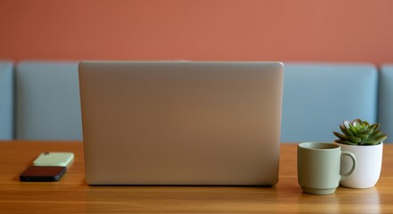A laptop is open on a table with a cup and a potted plant