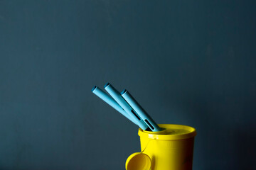 Couple of medicine syringe pen sticking out of toxic waste collection box container dark teal background. Studio medical equipment still life concept with auto-injector disposable devices. © Maarten Zeehandelaar