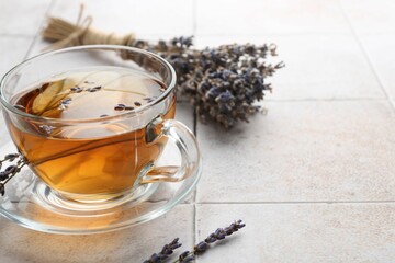 Aromatic lavender tea in glass cup and dry flowers on white tiled table, closeup. Space for text