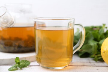 Aromatic mint tea and fresh leaves on white wooden table, closeup