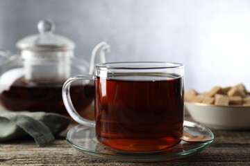 Aromatic black tea in cup and spoon on wooden table, closeup