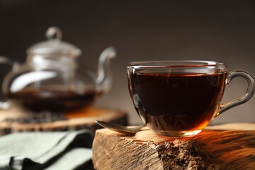 Aromatic black tea in cup on wooden snag, closeup