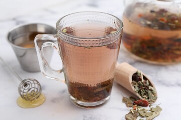 Delicious herbal tea with honey and dry leaves on white marble table, closeup
