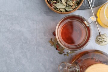 Delicious herbal tea with honey and dry leaves on grey table, flat lay. Space for text