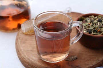Delicious herbal tea, honey and dry leaves on white table, closeup
