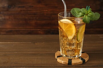 Refreshing iced tea with slices of lemon, lime, mint and drinking straw on wooden table, closeup. Space for text