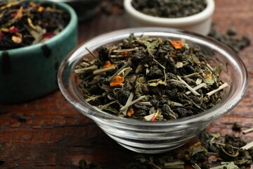 Different dry tea leaves in bowl on wooden table, closeup
