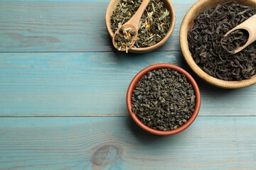 Different dry tea leaves in bowls on light blue wooden table, flat lay. Space for text