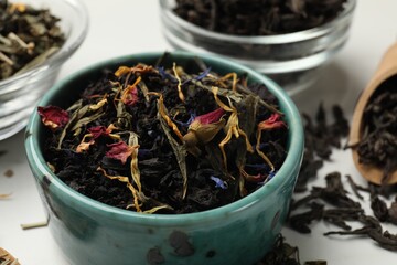 Different dry tea leaves in bowls on white table, closeup