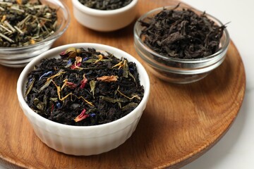 Different dry tea leaves in bowls on white table, closeup