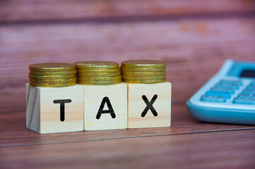TAX word on wooden cube with golden coins and calculator background. Taxation concept.